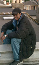 a handsome black man wearing a cap sitting outside on the roof of a building