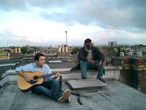 two men sitting outside on a roof ideating on a song