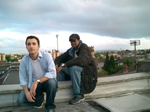 two men crouching on a roof against a suburban background